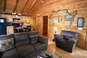 Ein Holzblockhaus-Interieur mit Essbereich, einer Couch, einem Sessel und einem Schild, das einen Waschraum kennzeichnet.