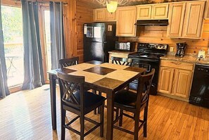 A kitchen with wooden cabinets, a black refrigerator, a stove, and a dining table with chairs. - Skinny Dippin 2 Bedroom Cabin (Pigeon Forge)
