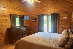 A wooden cabin bedroom with a bed, dresser, and a ceiling fan. - Skinny Dippin 2 Bedroom Cabin (Pigeon Forge)