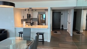 Een moderne keuken met een centraal eiland, roestvrijstalen apparatuur en een eetgedeelte met een glazen tafel en stoelen.
