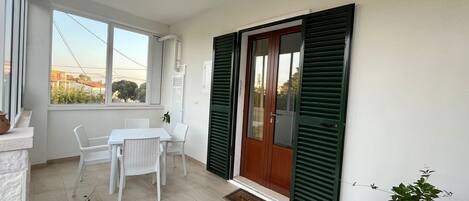 A small, bright room with a table and chairs, a door with green shutters, and a view of the outside.
