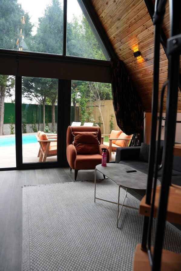 Un intérieur moderne avec une grande porte-fenêtre coulissante donnant sur une piscine, un fauteuil en cuir marron et un canapé gris.