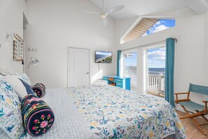 Quarto com cama, escrivaninha, cadeira, ventilador de teto e varanda com vista.