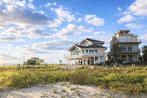A beachfront property with multiple houses, including a large house with a balcony and a smaller house in the foreground. - Beachfront 5BR | Hot Tub & Sauna | Wraparound Deck | Sleeps 14 | Pet-Friendly (Galveston)
