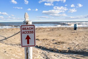 Placa de acesso à praia com uma seta apontando para cima, indicando o caminho.