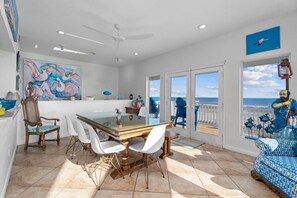 Uma sala de jantar com mesa de vidro, cadeiras brancas e vista para o oceano.