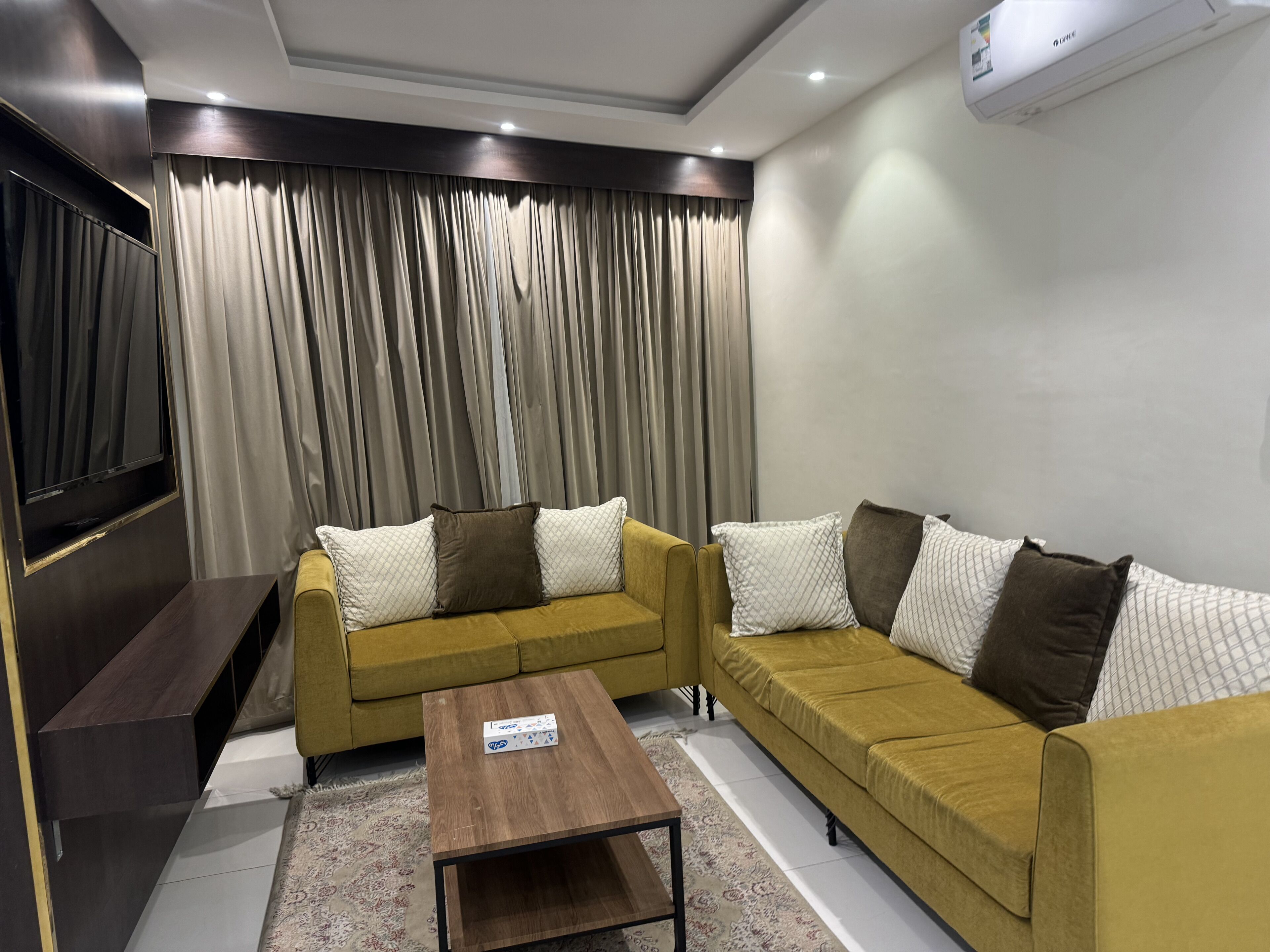 A living room with a yellow sofa set, a coffee table, and a flat-screen TV.