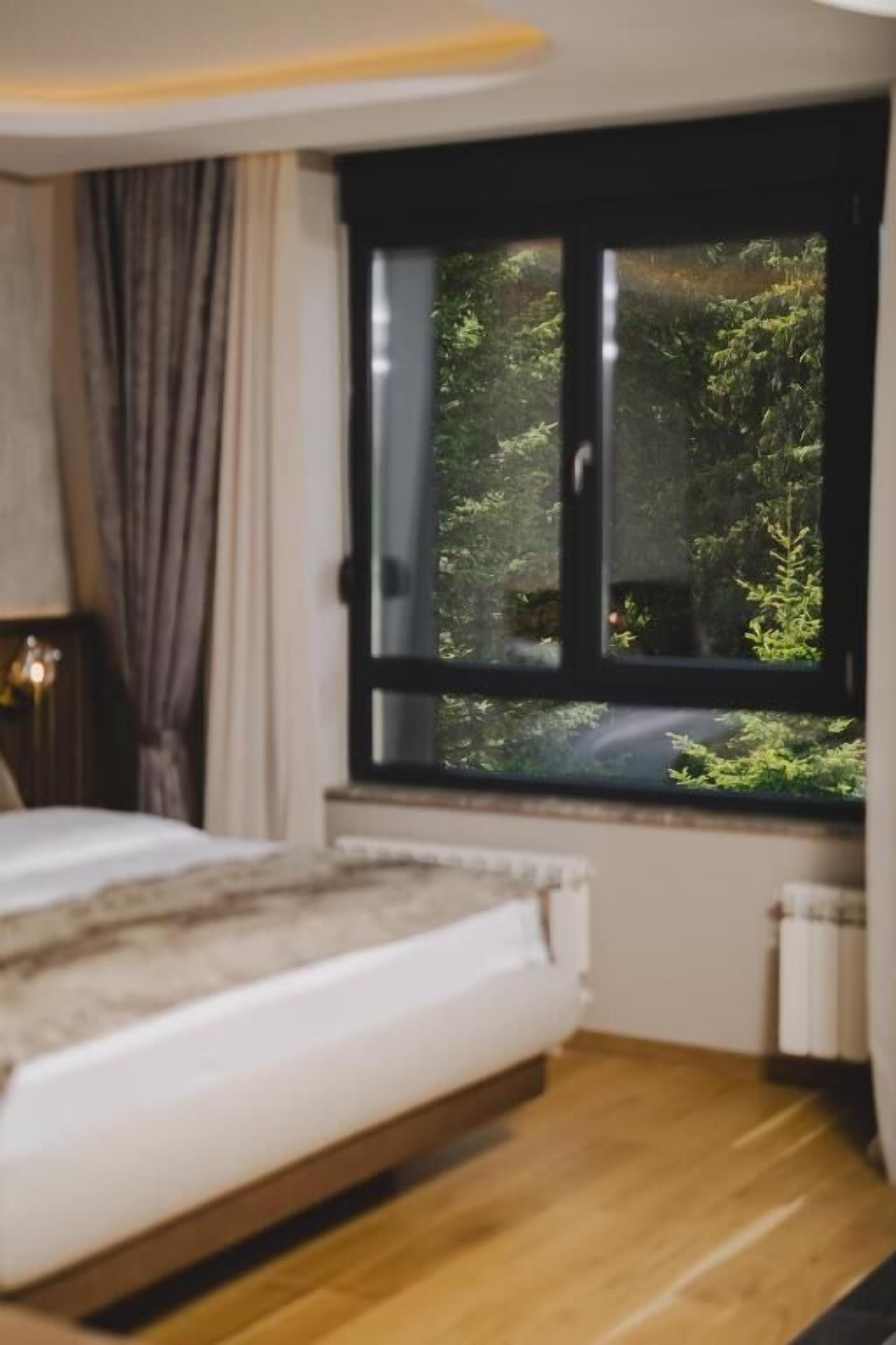 Et soveværelse med seng, et vindue med udsigt til grøn vegetation og en radiator.