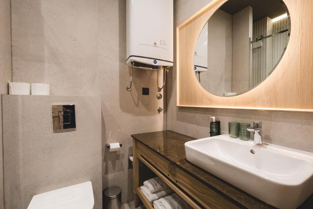 Un baño moderno con un lavabo blanco, tocador de madera, un espejo grande y un perchero para toallas.