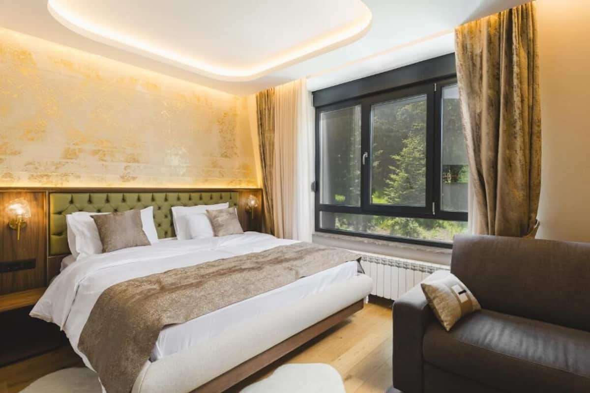 A bedroom with a bed, a window, a sofa, and a wall with a light fixture.