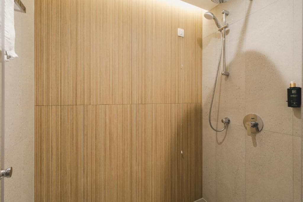 Un área de ducha con pared de panel de madera, un cabezal de ducha manual y un grifo empotrado en la pared.