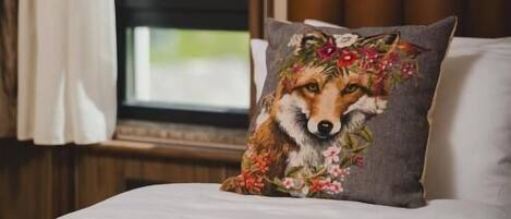 Una cama con un almohadón de diseño de zorro, una ventana con cortinas y vistas al verdor exterior.