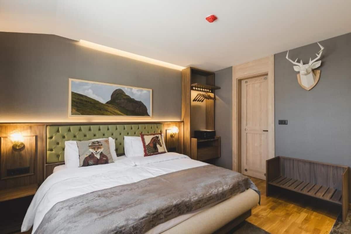 A bedroom with a bed, a mounted deer head, a framed landscape picture, and a bench.