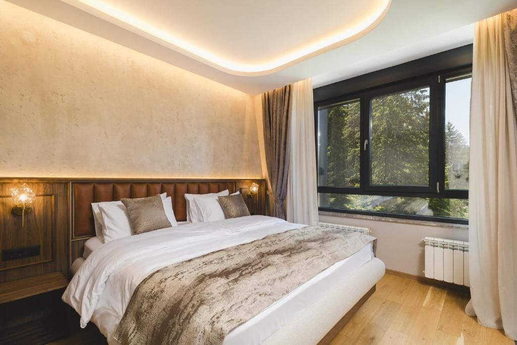 Ein Schlafzimmer mit einem großen Bett, einer Kopfteil, einem Fenster mit Vorhängen und einer Wandleuchte.
