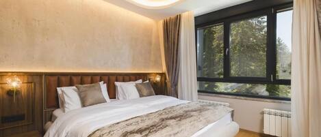 Ein Schlafzimmer mit einem großen Bett, einer Kopfteil, einem Fenster mit Vorhängen und einer Wandleuchte.