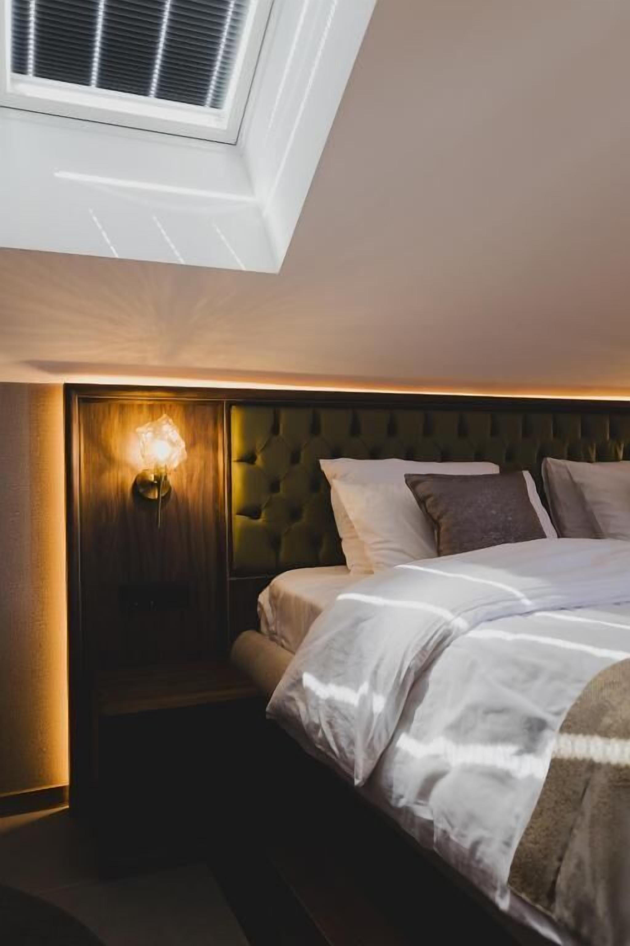 Une chambre à coucher comprenant un lit, une tête de lit, une lampe fixée au mur et un puits de lumière.