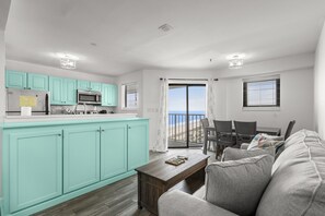 A modern kitchen with teal cabinets, a dining area with a gray sofa, and a view of the ocean through a sliding glass door. - T1614 at the Myrtle Beach Resort (Myrtle Beach)