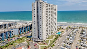 Ein Hochhaus-Hotel mit mehreren Stockwerken, einem Parkplatz und Blick auf den Strand.