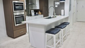 Cozinha moderna com eletrodomésticos embutidos, ilha central com banquetas e iluminação pendente.