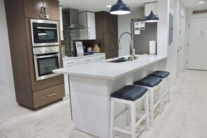 Eine moderne Küche mit integrierten Geräten, einer zentralen Kochinsel mit Barhocker und Pendelleuchten.