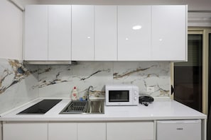 Une cuisine avec des meubles blancs, un four à micro-ondes, un évier et un égouttoir à vaisselle.