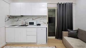 Una cocina compacta con armarios blancos, un microondas y un refrigerador pequeño.