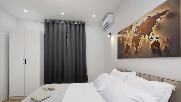 Un dormitorio con cama, cortinas blancas, un cuadro con un mapa del mundo y un equipo de aire acondicionado.