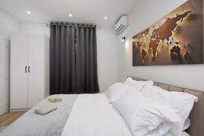 Une chambre à coucher avec un lit, des rideaux blancs, une décoration murale représentant une carte du monde et un appareil de climatisation.