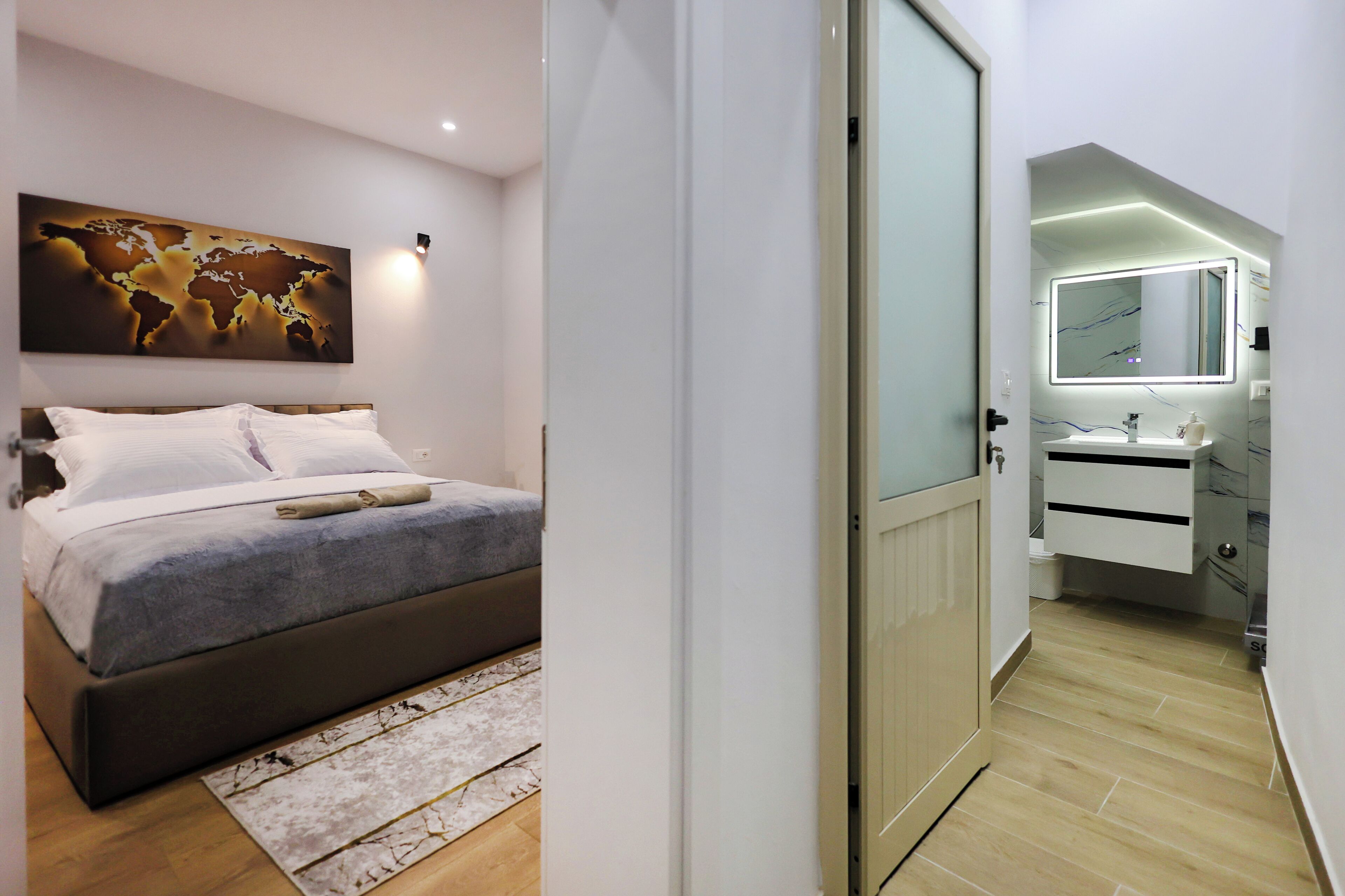 Une chambre à coucher moderne avec un lit, une œuvre d’art représentant une carte du monde, et une salle de bain avec un miroir et un lavabo.