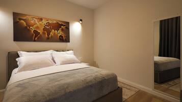 A neatly made bed with white linens, a world map artwork above it, and a large mirror reflecting the room.