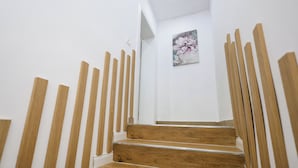 Una escalera de madera con barandales que lleva a una habitación con paredes blancas y un cuadro floral.