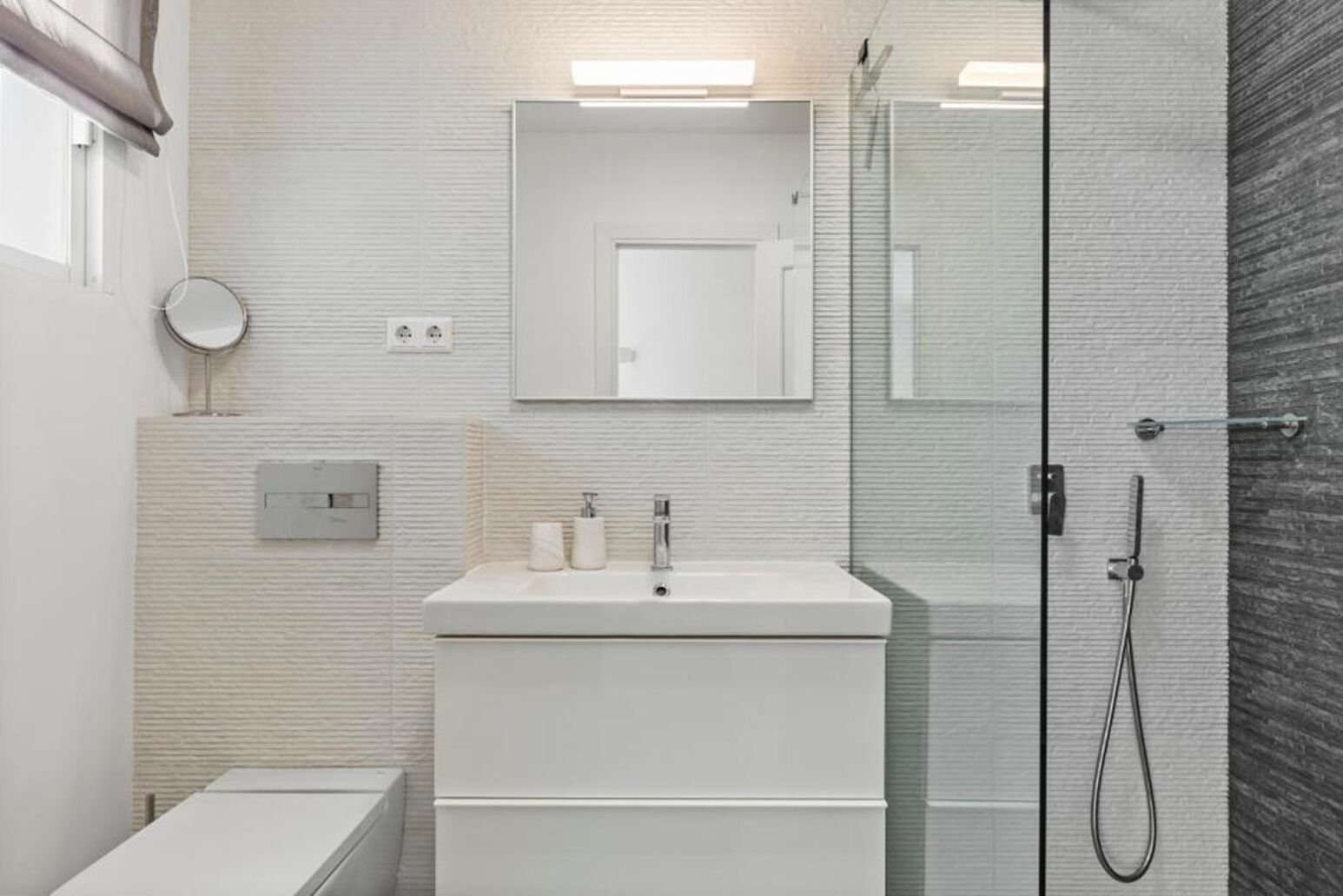 A modern bathroom with a glass shower enclosure, a white sink with a mirror above it, and a toilet to the left.