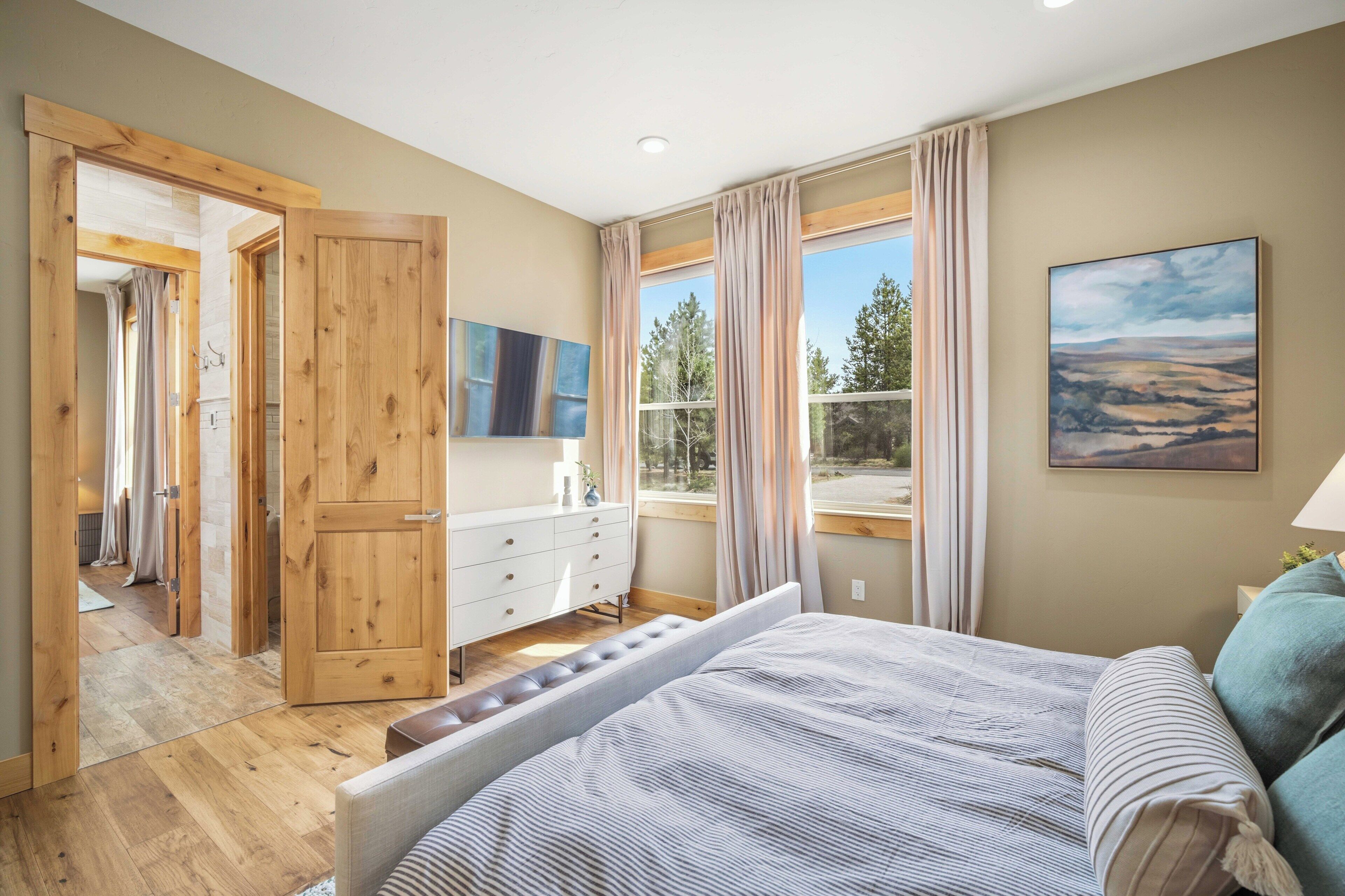 Une chambre à coucher avec un lit, une commode, une fenêtre avec des rideaux et un tableau accroché au mur.