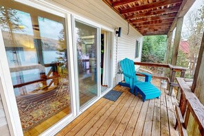 Eine Holzterrasse mit einem blauen Adirondack-Sessel, einer Glastür, die zu einem Raum führt, und einem Holzgeländer.