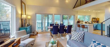 Amplia sala de estar con sofá, mesa de comedor y sillas, cocina con barra y balcón con vistas.