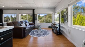 Een moderne woonkamer met een leren bank, een rond geweven vloerkleed en grote ramen met uitzicht op bomen.