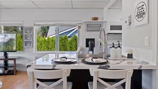 Een moderne keuken met een groot kookeiland, witte stoelen en uitzicht op groen.