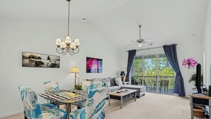 A spacious living room with a dining area, large windows, ceiling fans, and artwork on the walls. - River Crossing 332 Gated Community with Great Pool! New On Program! (North Myrtle Beach)