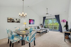 A spacious living room with a dining area, large windows, ceiling fans, and artwork on the walls. - River Crossing 332 Gated Community with Great Pool! New On Program! (North Myrtle Beach)