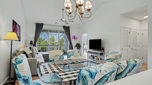 A modern living room with a sofa set, a dining table, a chandelier, and a television. - River Crossing 332 Gated Community with Great Pool! New On Program! (North Myrtle Beach)