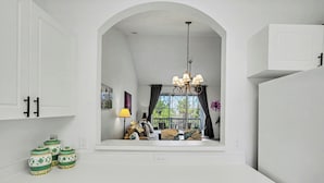 A white room with a large arched window, a chandelier, and a view of a balcony with outdoor furniture. - River Crossing 332 Gated Community with Great Pool! New On Program! (North Myrtle Beach)