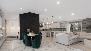 Cozinha moderna com armários brancos, área de jantar com piso de mármore e sala de estar com um amplo sofá modular.