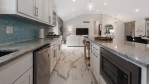 Uma cozinha moderna com armários brancos, bancada de mármore e lava-louças embutida.