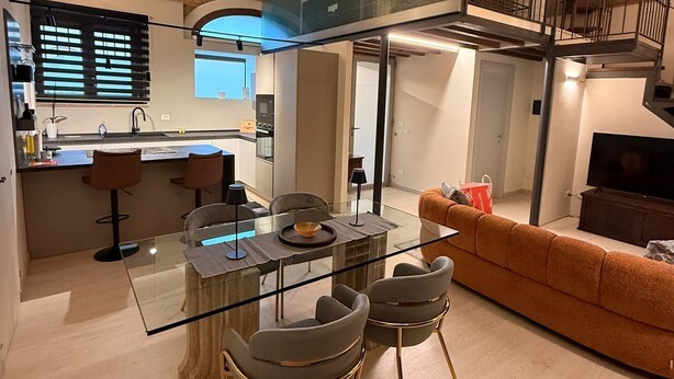 A modern kitchen with a central island, a dining area with a glass table and chairs, and a living area with a sofa and TV. - Eva House, 2-bedroom apartment with private parking space (Toscana)