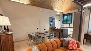 A modern living room with a brick ceiling, a sofa with patterned cushions, a dining area with a glass table, and a kitchen in the background. - Eva House, 2-bedroom apartment with private parking space (Toscana)