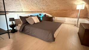 A bedroom with a brick ceiling, a bed with multiple pillows, a bedside table, a lamp, and a small desk. - Eva House, 2-bedroom apartment with private parking space (Toscana)