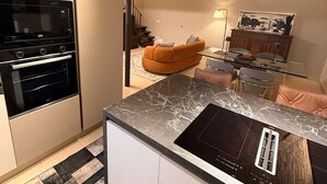 A modern kitchen with a built-in oven, a microwave, and a sleek island with a black induction cooktop. - Eva House, 2-bedroom apartment with private parking space (Toscana)