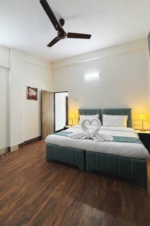 Een hotelkamer met een bed, een plafondventilator, een nachtkastje met lamp en een deur.