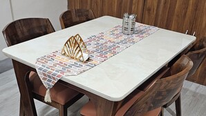 Une table à manger agrémentée d’un chemin de table à motifs, de chaises en bois et d’un porte-ustensiles en métal.