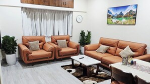 Un salon moderne avec deux canapés en cuir, une table basse et une table à manger avec des chaises. On y trouve également un ventilateur de plafond, une plante en pot et un tableau accroché au mur.